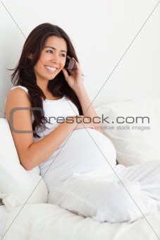 Good looking pregnant woman on the phone while lying on a bed