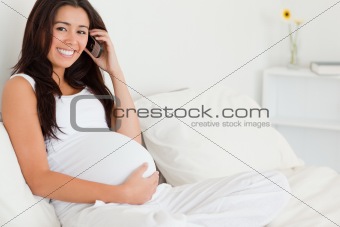 Pretty pregnant woman on the phone while lying on a bed