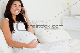 Gorgeous pregnant woman on the phone while lying on a bed