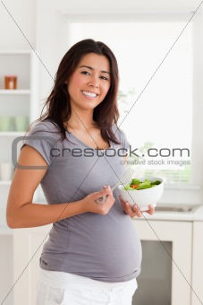Gorgeous pregnant woman holding a bowl of salad while standing