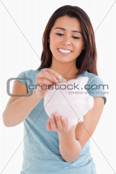 Beautiful woman inserting a coin in a piggy bank