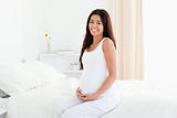 Beautiful pregnant woman touching her belly while sitting