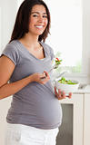 Pretty pregnant woman holding a bowl of salad while standing