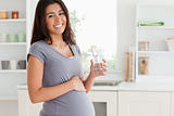 Attractive pregnant woman holding a glass of water while standing