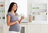 Gorgeous pregnant woman holding a glass of water while standing