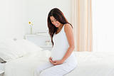 Pretty pregnant woman touching her belly while sitting on a bed