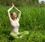 Beautiful young woman meditating in green grass