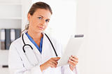 Charming doctor having a stethoscope around her neck pointing at a file looking at the camera