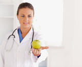 Good looking brunette doctor with stethoscope looking at an apple