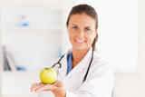 Doctor with stethoscope holding an apple looking at the camera