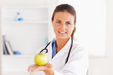 Doctor with stethoscope holding an apple looking into the camera