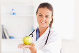 Smiling doctor with stethoscope holding an apple