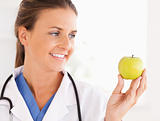 Close up of a smiling doctor with stethoscope looking at an apple