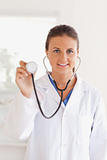smiling brunette doctor presenting a stethoscope looking into the camera
