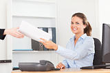 smiling businesswoman receiving a pile of paper looking into the camera