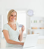 Blonde woman with credit card and notebook looks into camera