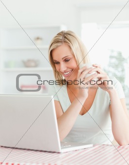 Close up of a woman holding cup of coffee looking at laptop 