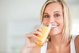 Close up of a smiling woman drinking orange juice in kitchen