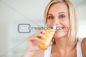 Close up of a smiling woman drinking orange juice in kitchen