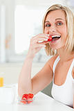 Young blonde woman sitting at table eats strawberries