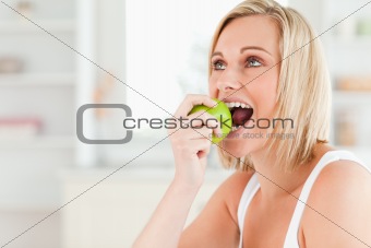 Young blonde woman sitting at table eating a green apple