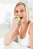 Young woman sitting at table eating a green apple while looking 