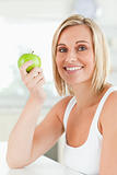 Young smiling woman holding a green apple looks into the camera