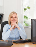 Smiling blonde woman with chin on her hands behind a desk