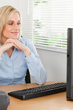 Charming blonde woman with chin on her hands behind a desk looki