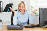 Smiling blonde woman sitting behind desk not having a clue what 