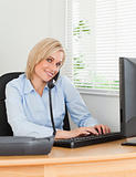 Smiling businesswoman on the phone while typing looks into camer