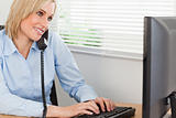 Smiling blonde businesswoman on the phone while typing looks at 