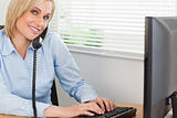 Smiling blonde businesswoman on the phone while typing looks int