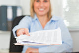 Smiling blonde businesswoman passing a paper looks into camera