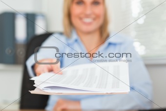 Smiling blonde businesswoman passing a paper looks into camera