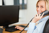 Young blonde businesswoman smiling into camera while on the phon