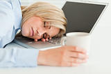 Gorgeous woman sleeping on her laptop with cup of coffee in hand