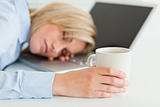 Gorgeous woman sleeping on her laptop holding cup of coffee