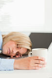 Gorgeous blonde woman sleeping on her laptop holding cup 