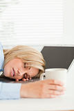 Gorgeous blonde woman sleeping on her notebook holding cup 