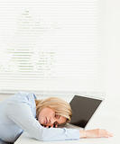 Cute blonde businesswoman sleeping on her notebook holding cup 