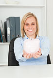 Cute blonde businesswoman holding a piggy bank 
