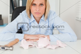 Sad woman sitting in front of an empty shattered piggy bank