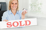 Blonde businesswoman showing miniature house and SOLD sign 