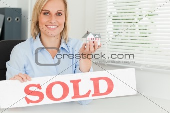 Blonde businesswoman showing miniature house and SOLD sign 