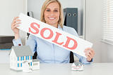 Blonde businesswoman showing SOLD sign looking into camera 