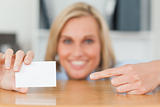 Businesswoman pointing at a card crouching behind her desk looks