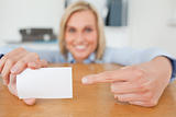 Blonde businesswoman pointing at a card crouching behind her desk