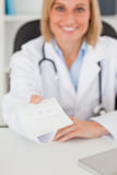 Smiling blonde doctor giving prescription looks into camera