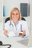 Smiling blonde doctor holding prescription and medicine looks in
